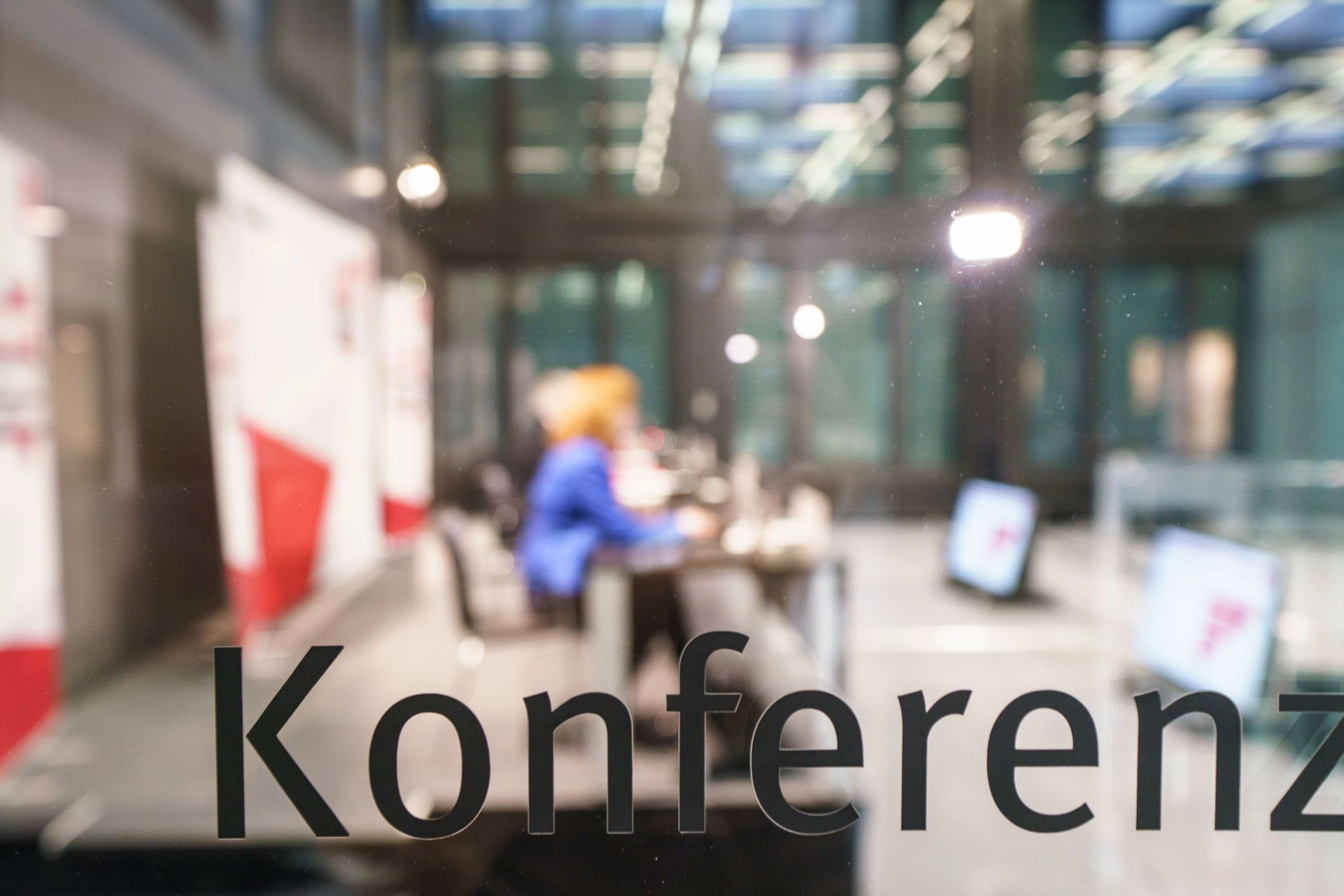 Glasscheibe mit der Aufschrift "Konferenz", dahinter unscharf ein Konferenzraum